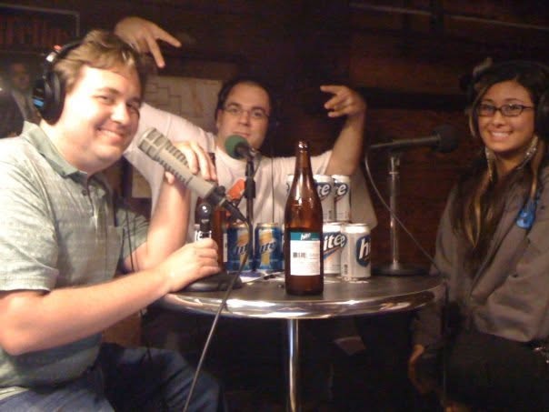 Salwin, Cioffi and Seena around a small table crowded with beer cans and bottles, mics in hand