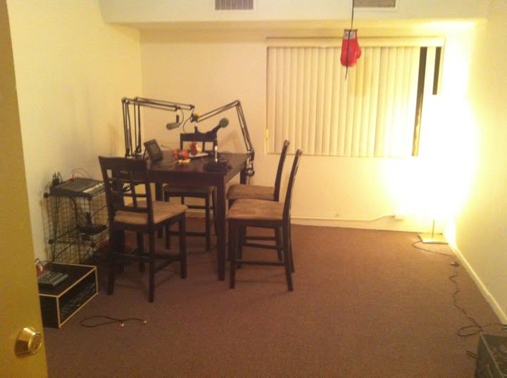The Laxdude Memorial Studio: high-top table with mic booms, chairs, mixing gear, and a red boxing glove hanging by the window